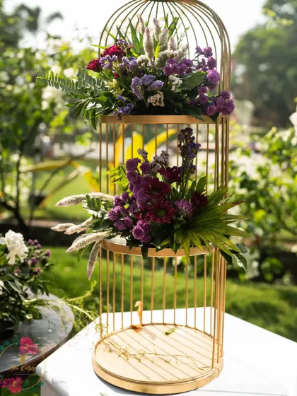 A tiered golden birdcage used as a decorative stand for lush floral arrangements, adding height and elegance to the decor.