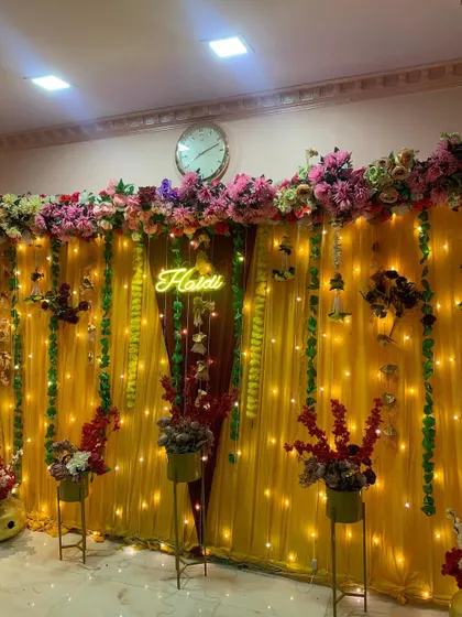 Another angle of the home Haldi setup, showing the floral arrangements on stands that flank the main backdrop, adding depth to the decor.