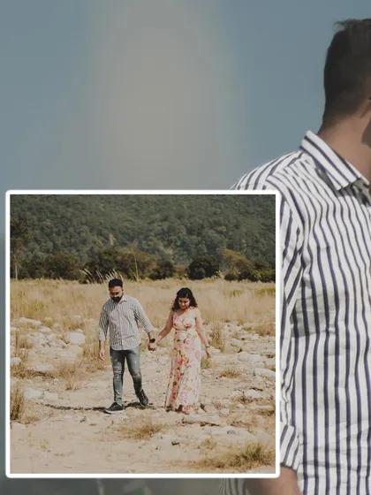 A candid moment from a pre-wedding shoot in a natural, open field. The couple is seen walking hand-in-hand, capturing the simple joy of being together.