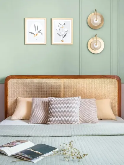 Comfort meets style in this bedroom detail. A woven cane headboard is paired with a two-tone wall featuring sage green paneling, creating a look that is both modern and rooted in Indian charm.
