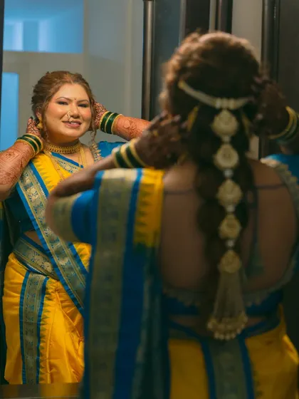 A look in the mirror before the big moment. This creative shot shows both the bride's happy reflection and the intricate details of her traditional braided hairstyle.