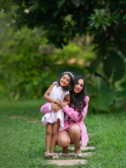 A mother crouches down to hug her older daughter in a beautiful garden setting. It's a perfect portrait of their loving bond.