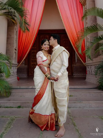 The groom sweetly kissing his bride's forehead as they stand before a grand entrance, a classic and timeless wedding portrait.