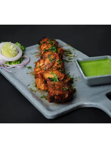 Juicy chicken tikka skewers arranged on a modern grey platter with mint chutney. The dark background and focused lighting make the colors pop, creating a premium look for an Indian restaurant.