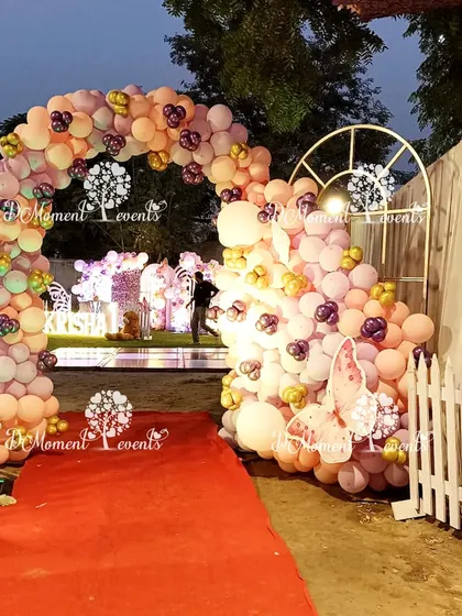 A red carpet entrance through a whimsical arch of pastel balloons and butterfly cutouts, leading guests into the magical party space.