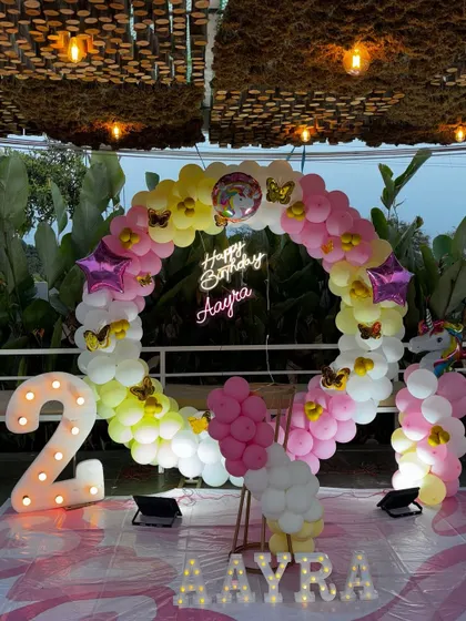 A dreamy Unicorn theme for a second birthday. This outdoor setup features a circular balloon arch in pastel rainbow colors, a light-up number '2', and unicorn and butterfly details.