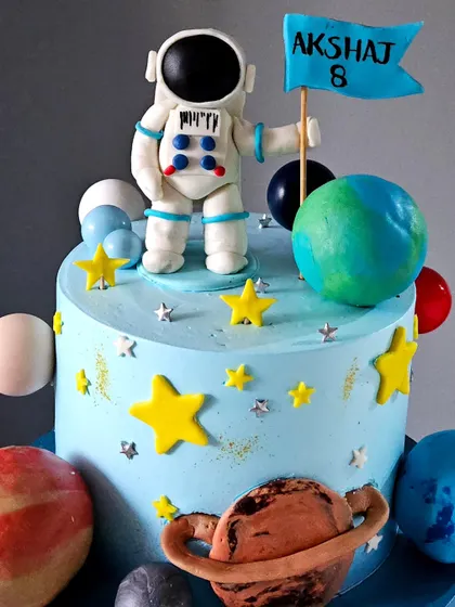 A close-up of the handmade astronaut figurine. You can see the intricate details of his suit and the personalized flag he's holding, making it a special topper for the birthday boy.