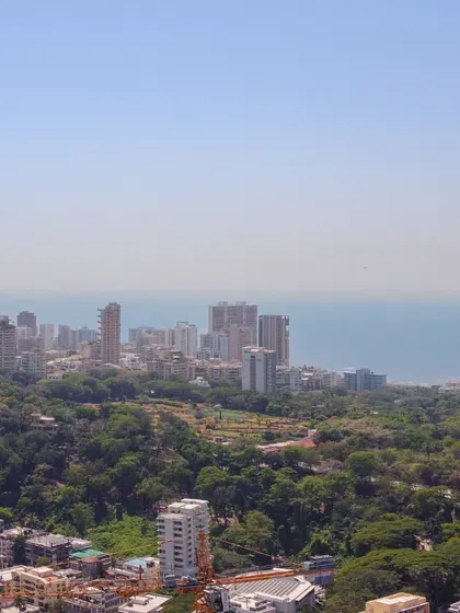 An aerial view of Malabar Hill's lush greenery contrasting with the dense urban development of Mumbai against the sea.