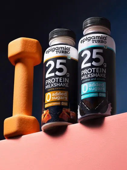 This shot connects Epigamia's protein milkshake directly to fitness by including a dumbbell. The composition uses strong lines and color blocking to create a modern, health-focused lifestyle image.
