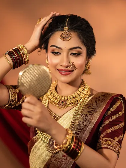 A happy bride-to-be trying on a classic temple jewellery set. This one features a beautiful coin haaram and a detailed choker, paired with a traditional nose ring and maang tikka.