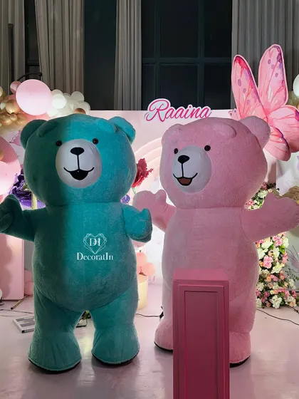 The friendly teal and pink teddy bear mascots posing in front of the butterfly-themed birthday backdrop.