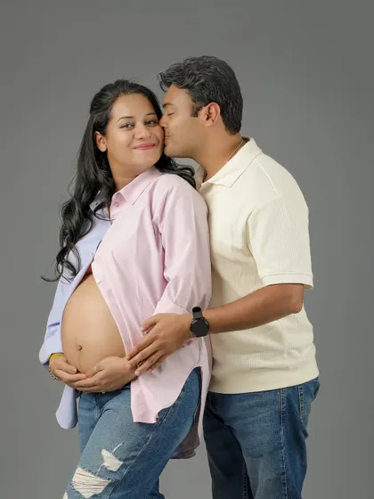 A sweet and casual couple portrait. The husband-to-be gives his wife a gentle kiss on the cheek as she smiles, showing her beautiful bare baby bump.