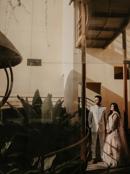 A wide, architectural shot of the couple in a modern setting. The interplay of light, shadow, and structural lines creates a dramatic and stylish pre-wedding portrait.