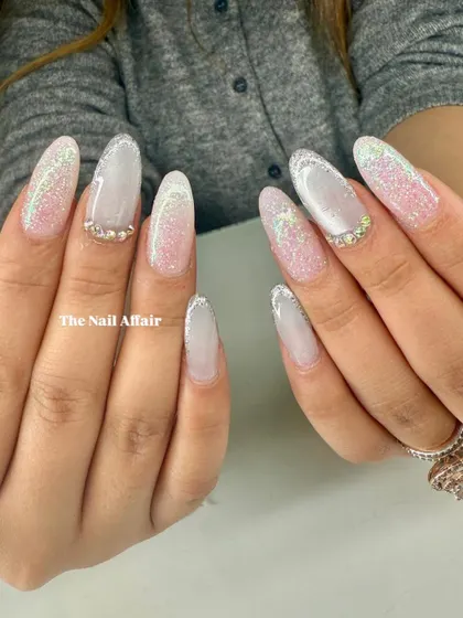 An elegant and glamorous set of long almond nails, featuring a soft ombré base with a sparkling glitter fade and rhinestone accents.