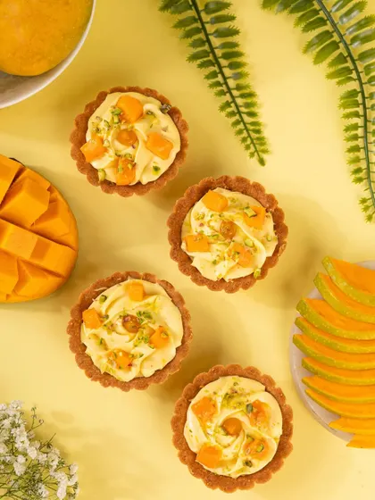 A flat lay of mini mango tarts, arranged beautifully on a bright yellow background to celebrate mango season.
