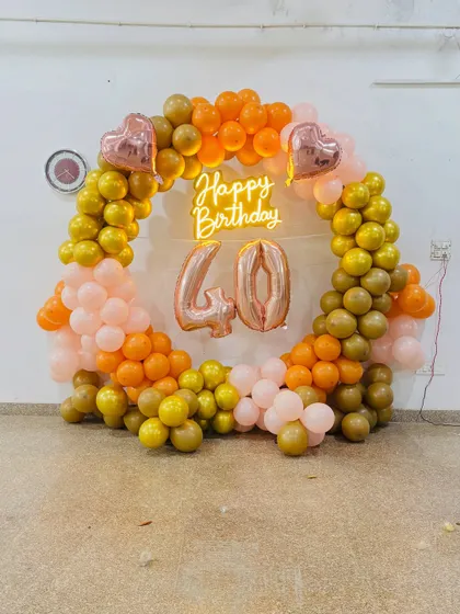 A warm and inviting 40th birthday decoration. The circular balloon arch in shades of orange and gold with a neon sign and marquee numbers is perfect for celebrating a milestone.