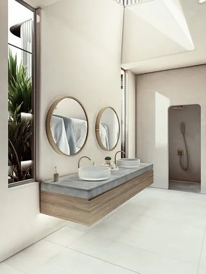 A bathroom in a Pavilion home, where filtered light enters through a courtyard and skylight. The space is designed to feel expansive, with a floating vanity and separate shower stalls that maintain an open feel.