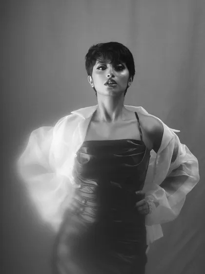 A confident black and white portrait of a model in a dark dress and a sheer white shirt. The soft, glowing effect around her adds a touch of ethereal drama to this fashion-forward shot.