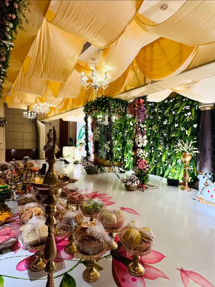 A view of our Picuwari decor for a half-saree ceremony, featuring a custom-painted floor, a lush green wall, and an array of traditional sweets and gifts beautifully arranged.