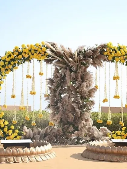 An alfresco Haldi decor setup with a circular floral arch made of yellow marigolds and pampas grass, overlooking a serene view. Perfect for a destination wedding.