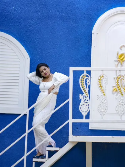 A stylish portrait of a woman in a white saree against a vibrant blue wall, taken during her birthday photoshoot.