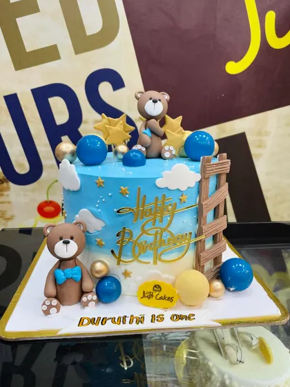 A dreamy 2.5kg teddy bear cake with a blue sky, clouds, and stars theme for a first birthday.