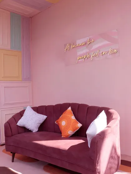 A cozy seating nook with a pastel-paneled wall and a romantic neon sign, combining modern art with comfortable design.