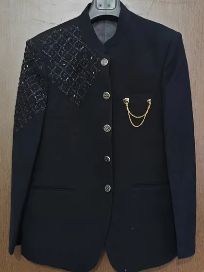 A closer look at this black Jodhpuri-style suit jacket. It features a mandarin collar, intricate shoulder beading, and a pocket chain for a touch of regal flair.