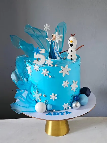 A magical Frozen-themed cake for a 5th birthday. This design features a vibrant blue color, edible snowflakes, translucent sugar sails, and handcrafted figurines of both Elsa and Olaf.