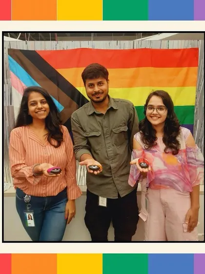 A group of colleagues posing with their painted pebbles in front of a Pride flag. This activity combines creativity with a powerful message of diversity and inclusion.