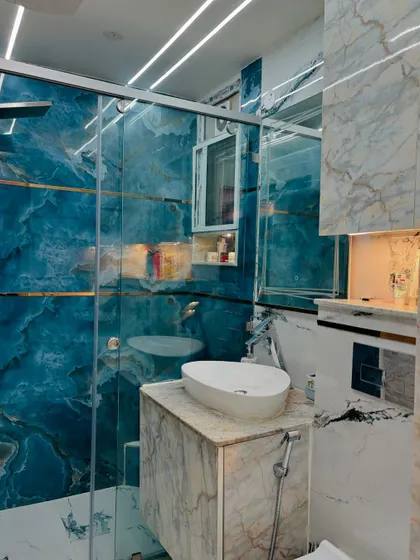 A stunning bathroom renovation featuring a bold blue marble-finish tile. The design includes a glass shower partition and a compact vanity, creating a luxurious and modern look.