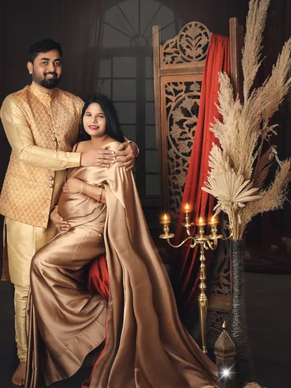 Draped in a luxurious golden satin saree, this mom-to-be looks like royalty. The studio setup with the carved screen and warm lighting enhances the traditional and elegant theme of the shoot.