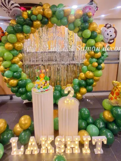 A jungle animal theme for a second birthday. This setup features a circular balloon arch with a tinsel backdrop, animal foil balloons, and a light-up name and number.