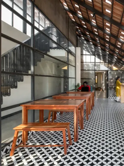 This is the cafeteria area within the Earthen Spirit co-living space, located on the open terrace. We used simple wooden furniture and patterned cement tiles to create a welcoming community area. The glass wall provides a clear view of the new double-height staircase, making the entire space feel connected and expansive.