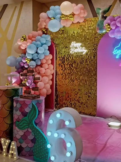 A side view of a mermaid-themed sixth birthday, showing the shimmering gold backdrop and pastel balloon arch.