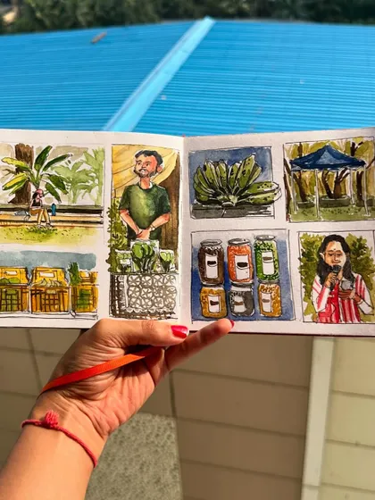 Holding up my farmer's market sketchbook spread against a bright blue roof, making the watercolour colours pop.