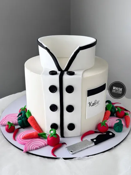 A cake for a budding chef. This design is shaped like a chef's coat and is surrounded by tiny, handcrafted vegetables and a miniature cleaver.