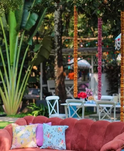 A comfortable and stylish seating area for a garden Mehendi party, with a plush red sofa and colorful cushions.