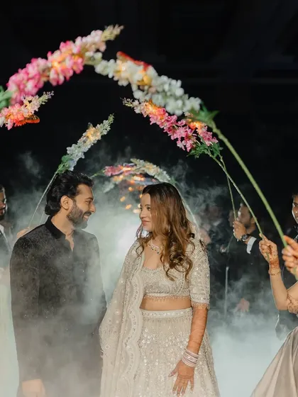 The couple's entry through a tunnel of flowers held by their friends, with smoke creating a magical, ethereal effect.
