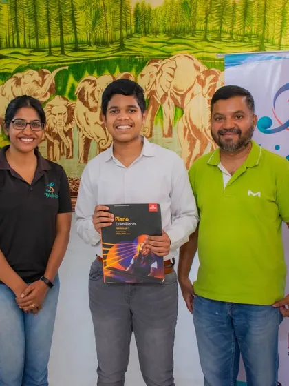 A student holding his ABRSM piano exam book stands with his teachers.