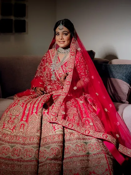 The bride seated, looking like royalty in her magnificent red lehenga. The full view showcases the grandeur of her outfit and the elegance of her overall look.