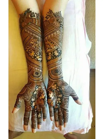 A stunning portrait mehendi with intricate details on the bride's face and jewelry. The arms are adorned with peacock and floral patterns.