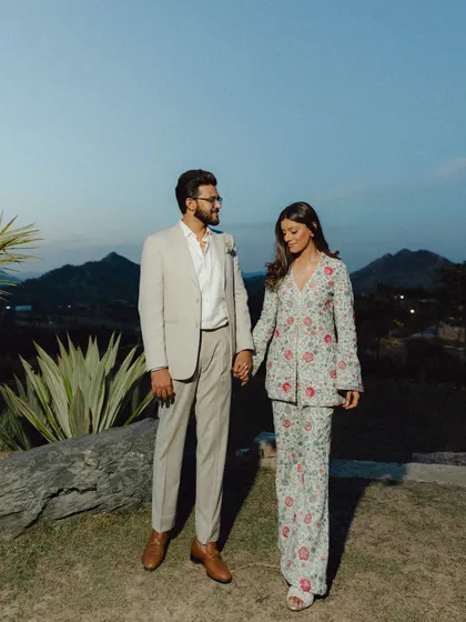 A stylish, full-length portrait of Mouli and Jaymit against the backdrop of the Udaipur mountains at dusk. Their coordinated floral outfits are a standout detail.