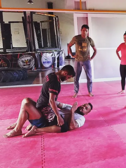 Here, two students are drilling a guard pass. This exercise teaches the person on top how to navigate their opponent's legs to gain a more dominant position, a key aspect of grappling.