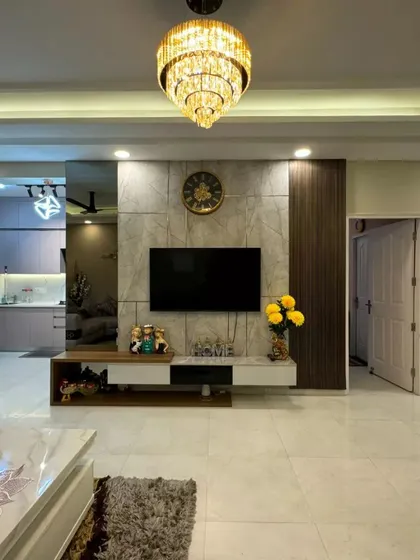 The living area of the Gurgaon home, showing a modern TV unit with a marble-effect back panel and a stunning tiered chandelier that serves as a focal point.