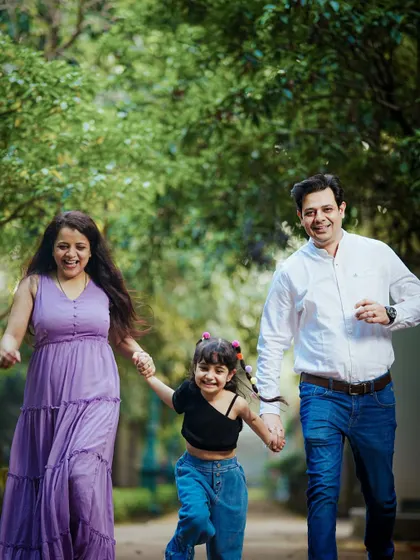 An action shot of a family holding hands and running joyfully towards the camera along a park path.