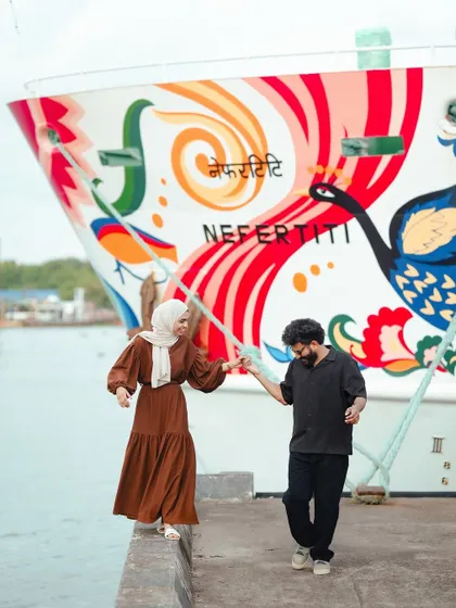 A playful moment captured as the couple walks along the edge of a pier, with the vibrant 'Nefertiti' ship adding a unique backdrop.