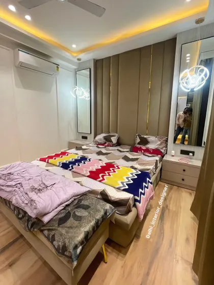 This bedroom design features a floor-to-ceiling upholstered headboard with brass inlay details. The matching bedside tables and hanging lights complete the symmetrical and luxurious look.