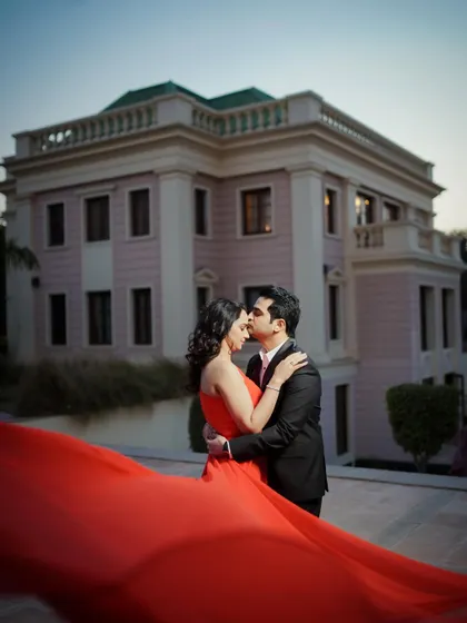 A classic pre-wedding portrait with a grand architectural backdrop. The flowing red gown adds a pop of color and drama to this romantic embrace.