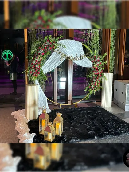 A complete view of this circular photo booth, designed with red roses, white drapes, lanterns, and modern pedestals for a stylish photo opportunity.
